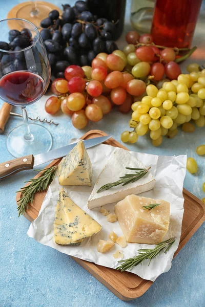Diferentes tipos de queso con uvas maduras y copa de vino tinto en mesa de color — Foto de Stock