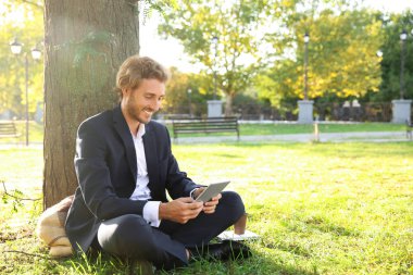 Yakışıklı genç işadamı ile tablet Pc Park yeşil çimenlerin üzerinde dinlenme