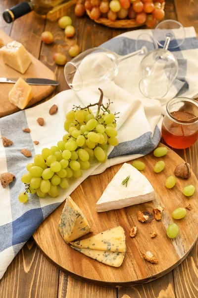 Tabla de madera con queso y uvas frescas maduras en la mesa — Foto de Stock