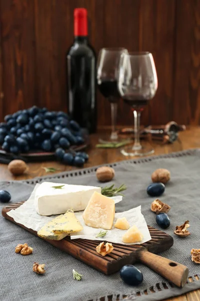 Placa de madeira com diferentes tipos de queijo, uvas maduras e nozes na mesa — Fotografia de Stock