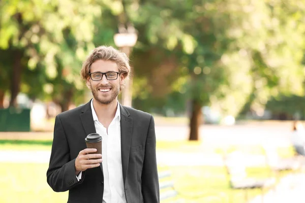 Guapo joven hombre de negocios con café descansando en el parque — Foto de Stock