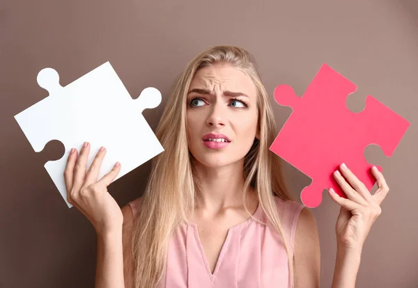 Troubled giovane donna con pezzi di puzzle su sfondo di colore — Foto Stock