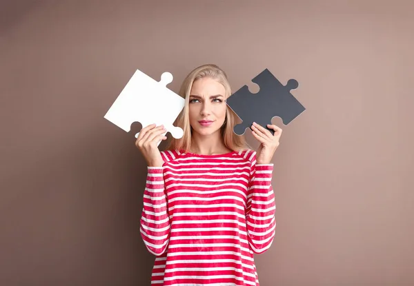 Giovane donna riflessivo con pezzi di puzzle su sfondo di colore — Foto Stock