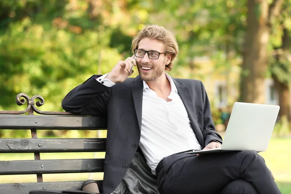 Handsome young businessman talking by mobile phone in park Royalty Free Stock Images