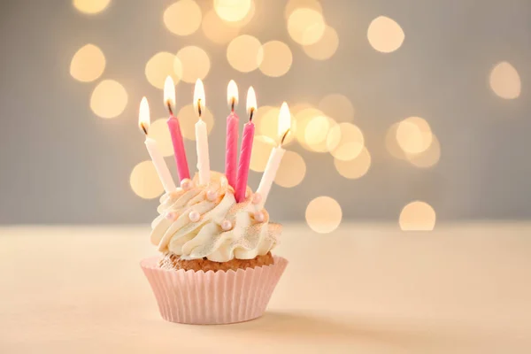 Delicioso cupcake de cumpleaños con velas encendidas en la mesa contra luces borrosas — Foto de Stock