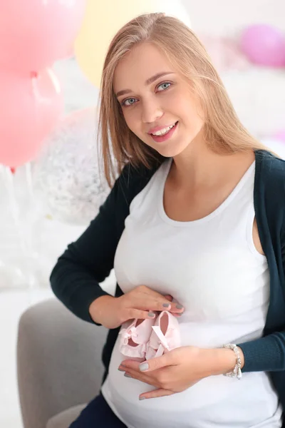 Beautiful pregnant woman with baby booties at home — Stock Photo, Image