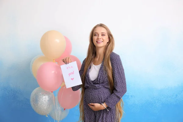 Schöne schwangere Frau mit Karte und Luftballons auf farbigem Hintergrund — Stockfoto