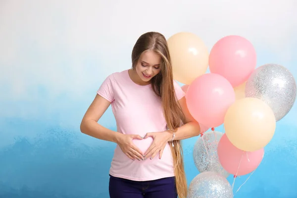 Красивая беременная женщина с воздушными шарами на цветном фоне — стоковое фото