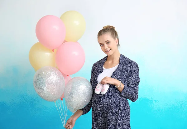 Szép terhes nő Babacipők és hőlégballonok, színes háttérrel — Stock Fotó