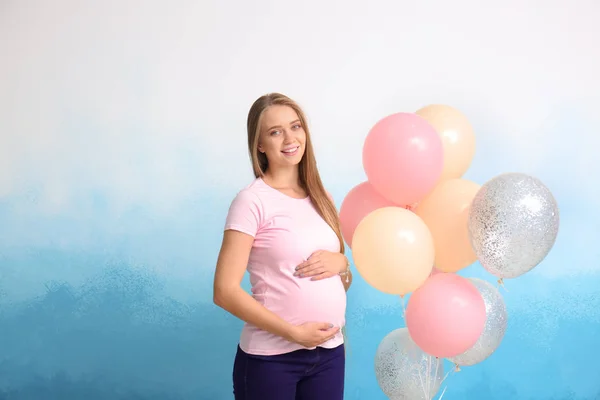 Schöne schwangere Frau mit Luftballons auf farbigem Hintergrund — Stockfoto