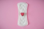 Menstruationspolster mit rotem Herz auf farbigem Hintergrund