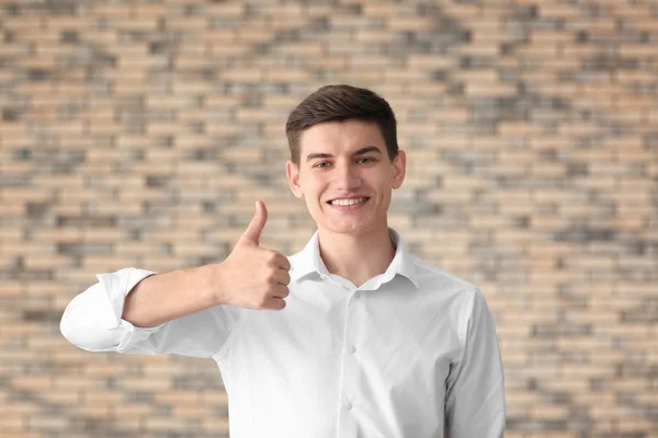 Portrait of handsome young man showing thumb-up gesture against brick wall — Stock Photo, Image