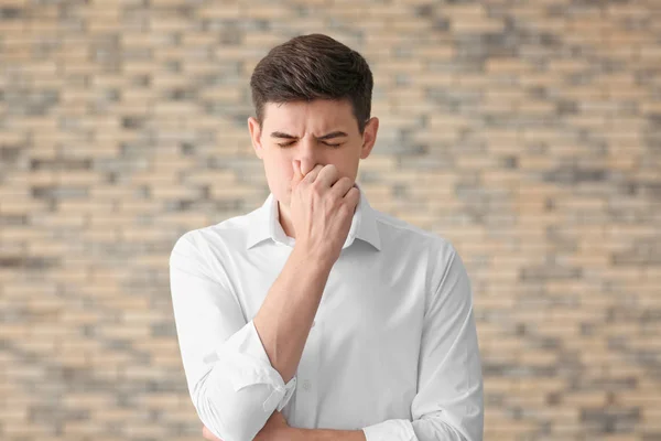 Portrait of handsome young man pinching nose against brick wall — Stock Photo, Image