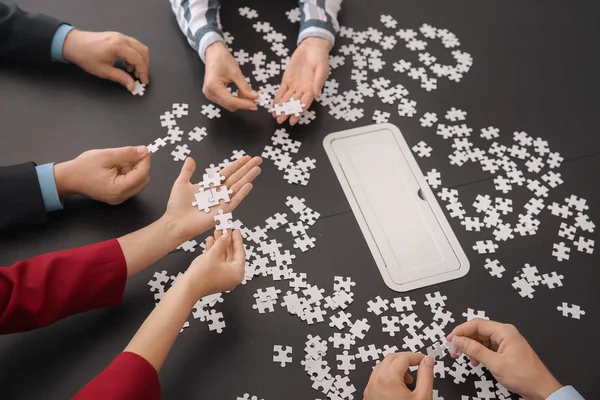 Business team assembling puzzle on dark table