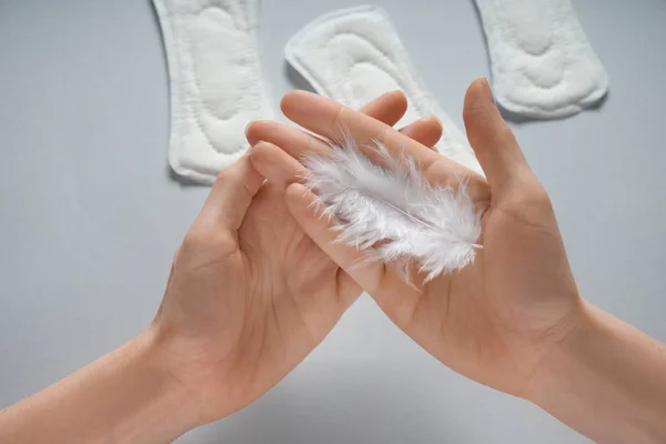 Mujer con plumas y almohadillas menstruales sobre fondo gris, primer plano —  Fotos de Stock