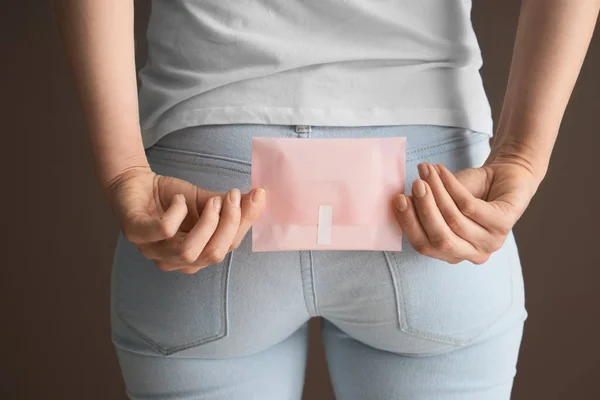 Woman holding menstrual pad behind her back on color background — Stock Photo, Image