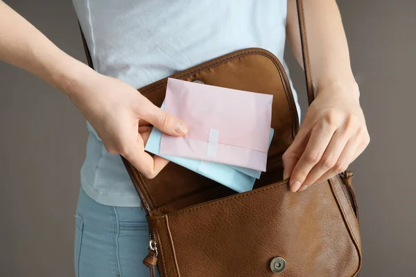 Frau steckt Menstruationspolster in Tasche auf grauem Hintergrund — Stockfoto