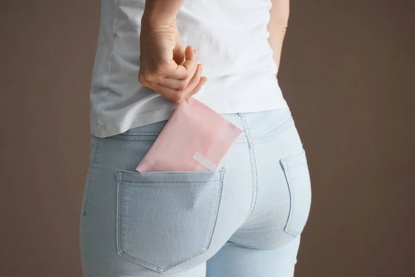 Woman putting menstrual pad into pocket on color background — Stock Photo, Image