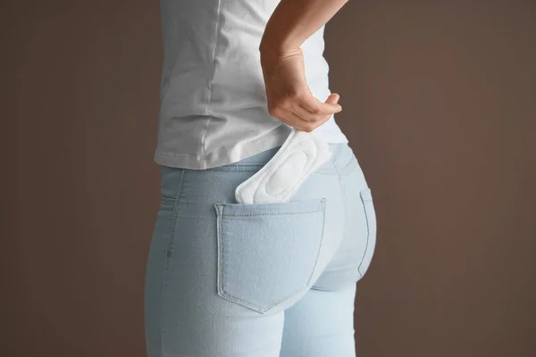 Woman putting menstrual pad into pocket on color background — Stock Photo, Image