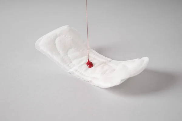 Menuang cat merah ke pad menstruasi pada latar belakang abu-abu — Stok Foto