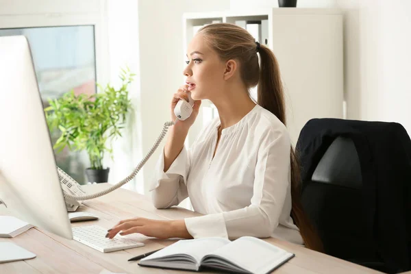 Beautiful female secretary talking on telephone in office — Stock Photo, Image