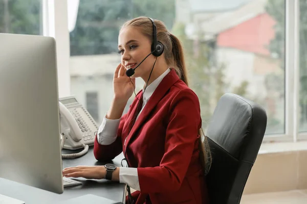 Hermosa secretaria hablando a través de auriculares en la oficina —  Fotos de Stock