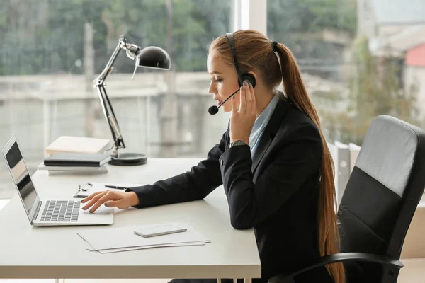 Hermosa secretaria hablando a través de auriculares en la oficina —  Fotos de Stock