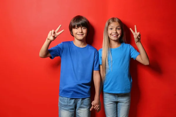 Menino e menina em camisetas mostrando gesto de vitória no fundo de cor — Fotografia de Stock