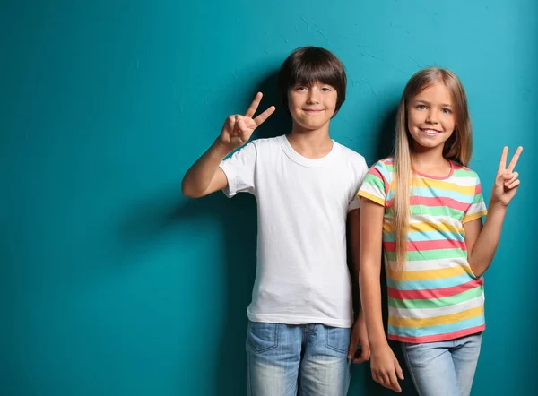 Boy and girl in t-shirts showing Victory gesture on color background — Stock Photo, Image