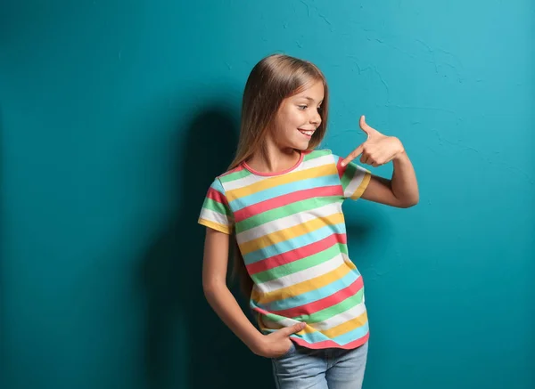 Smiling little girl pointing at her t-shirt on color background — Stock Photo, Image