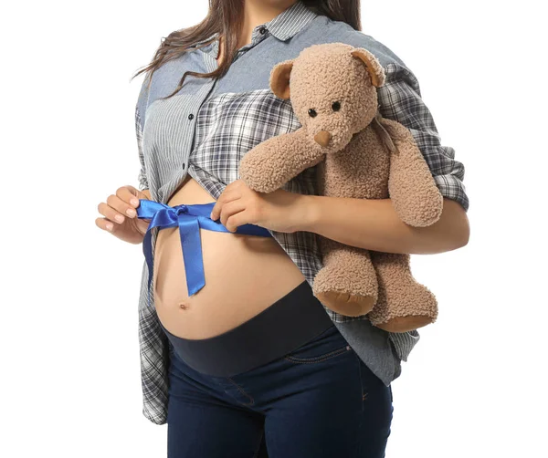 Mulher grávida bonita com urso de brinquedo e fita azul em sua barriga contra fundo branco — Fotografia de Stock