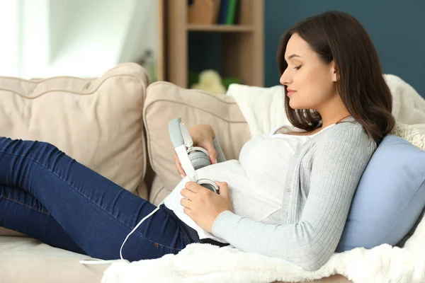 Piękne kobiety w ciąży, umieszczenie słuchawki na brzuch podczas odpoczynku w domu — Zdjęcie stockowe
