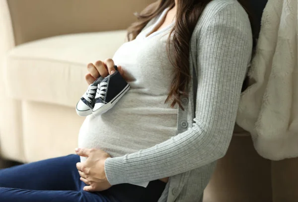 Красива вагітна жінка з дитячими пінетками вдома — стокове фото