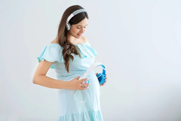 Frumoasă femeie însărcinată care pune căști pe burtă pe fundal luminos — Fotografie, imagine de stoc