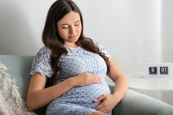 Smuk gravid kvinde sidder på sofaen derhjemme - Stock-foto