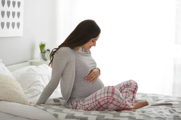 Beautiful pregnant woman sitting on bed at home — Stock Photo, Image