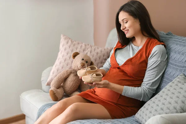 Mulher grávida bonita com botas de bebê em casa — Fotografia de Stock