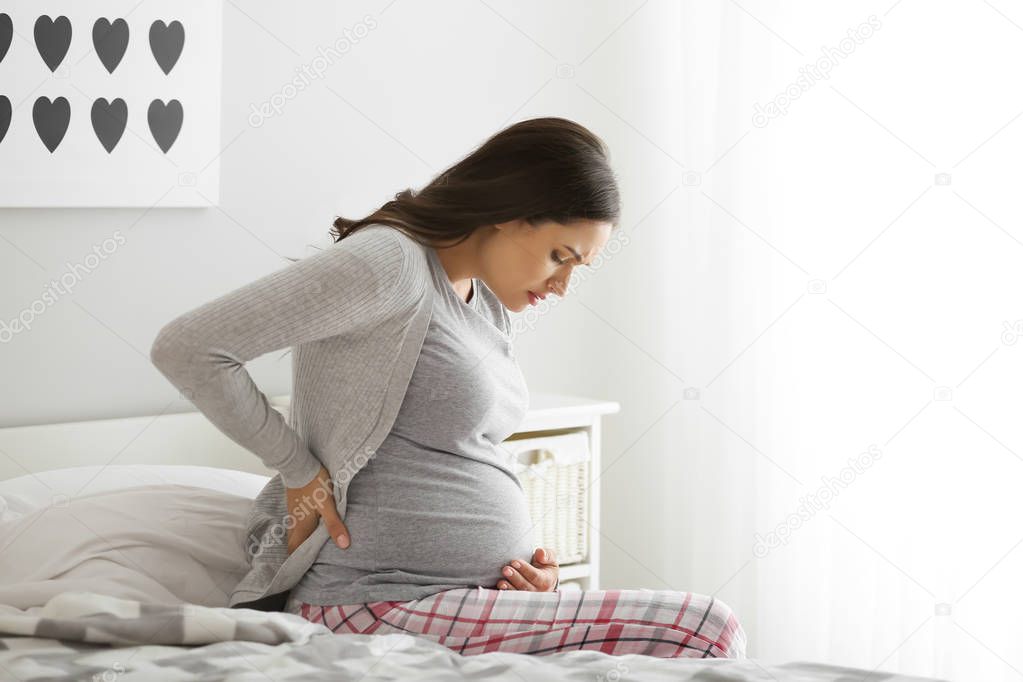 Pregnant woman suffering from pain in bedroom