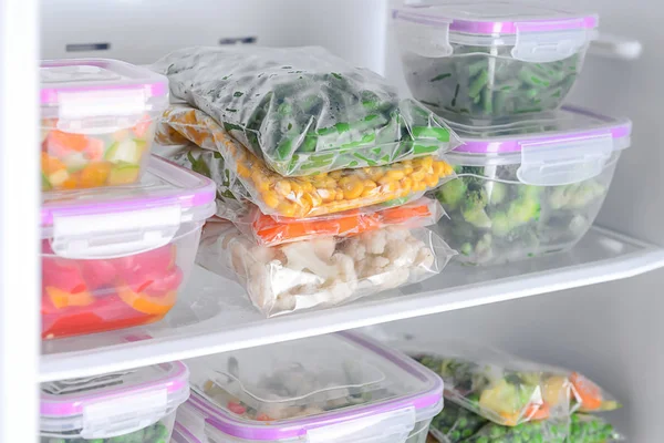 Containers and plastic bags with frozen vegetables in refrigerator — Stock Photo, Image