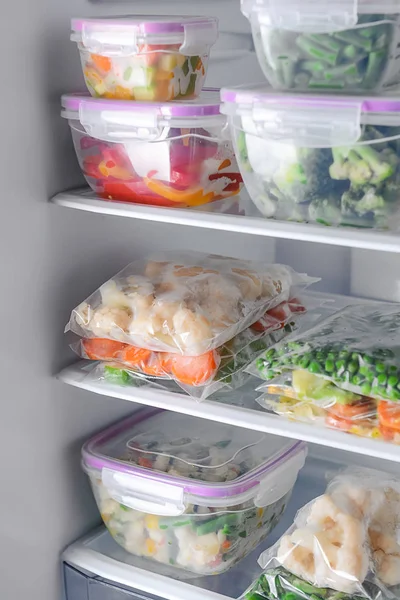 Containers and plastic bags with frozen vegetables in refrigerator — Stock Photo, Image