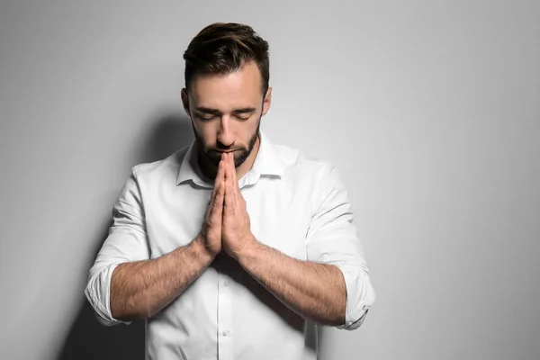 Religious young man praying to God on light background — Stock Photo, Image