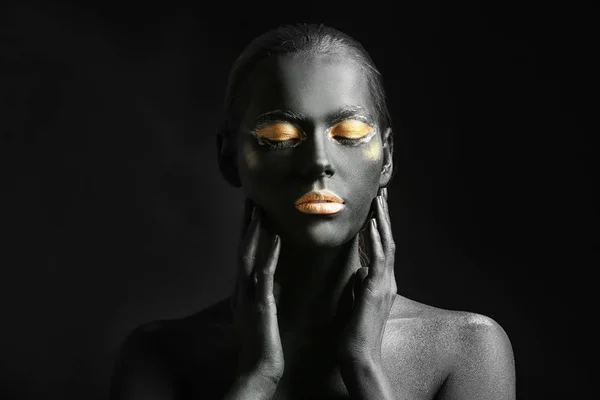 Beautiful woman with black and golden paint on her body against dark background — Stock Photo, Image