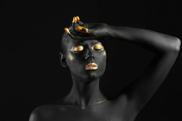 Piękna kobieta z czarno-złotą farbą na jej ciele na ciemnym tle — Zdjęcie stockowe