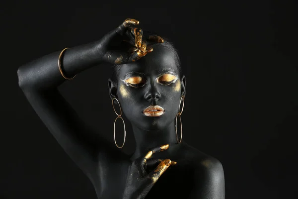 Piękna kobieta z czarno-złotą farbą na jej ciele na ciemnym tle — Zdjęcie stockowe