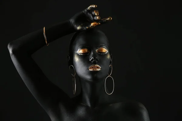 Vacker kvinna med svart och gyllene färg på kroppen mot mörk bakgrund — Stockfoto