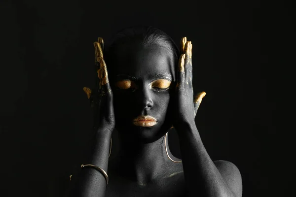 Beautiful woman with black and golden paint on her body against dark background — Stock Photo, Image