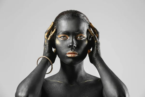 Mulher bonita com tinta preta e dourada em seu corpo contra fundo claro — Fotografia de Stock