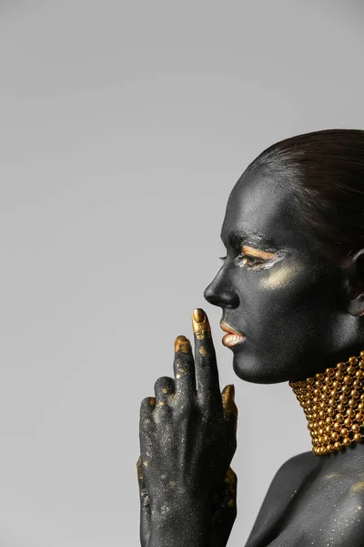 Beautiful woman with black and golden paint on her body against light background — Stock Photo, Image