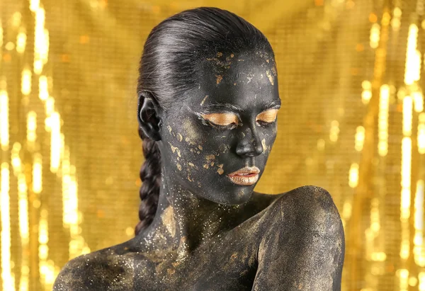 Beautiful woman with black and golden paint on her body against color background — Stock Photo, Image