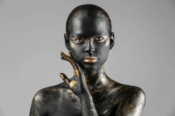 Beautiful woman with black and golden paint on her body against light background — Stock Photo, Image